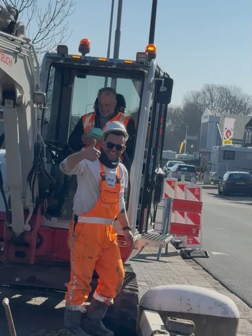 Grondwerker steekt zijn duim op bij een uitgegraven sleuf naast een graafmachine
