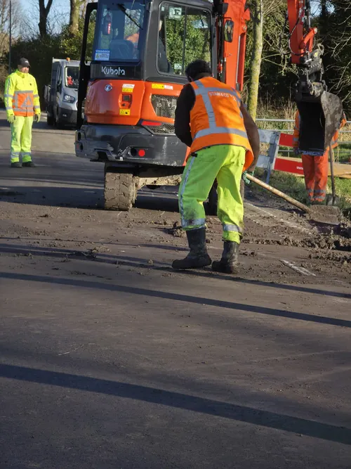 Grondwerker aan het werk bij een minigraver op een weg met opengebroken asfalt